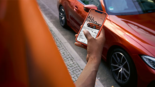 Woman holding smartphone standing in front of a BMW car